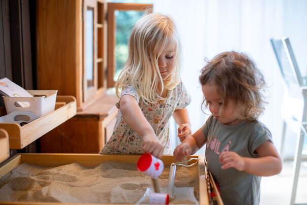2 Kinder beim Spielen im Sandkasten. Der Spiilruum ist nicht nur ein Raum zum Spielen und Lernen, sondern auch ein Indoorspielplatz für Gross und Klein.